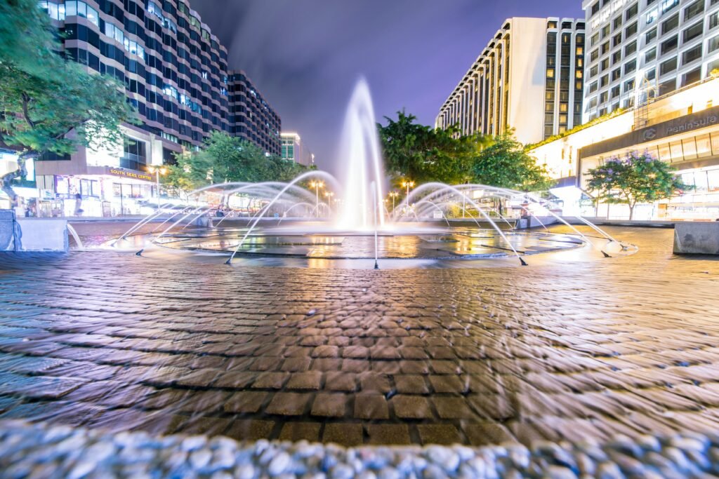 Capture of a city fountain illuminated at night, set against modern city buildings and vibrant street lights.